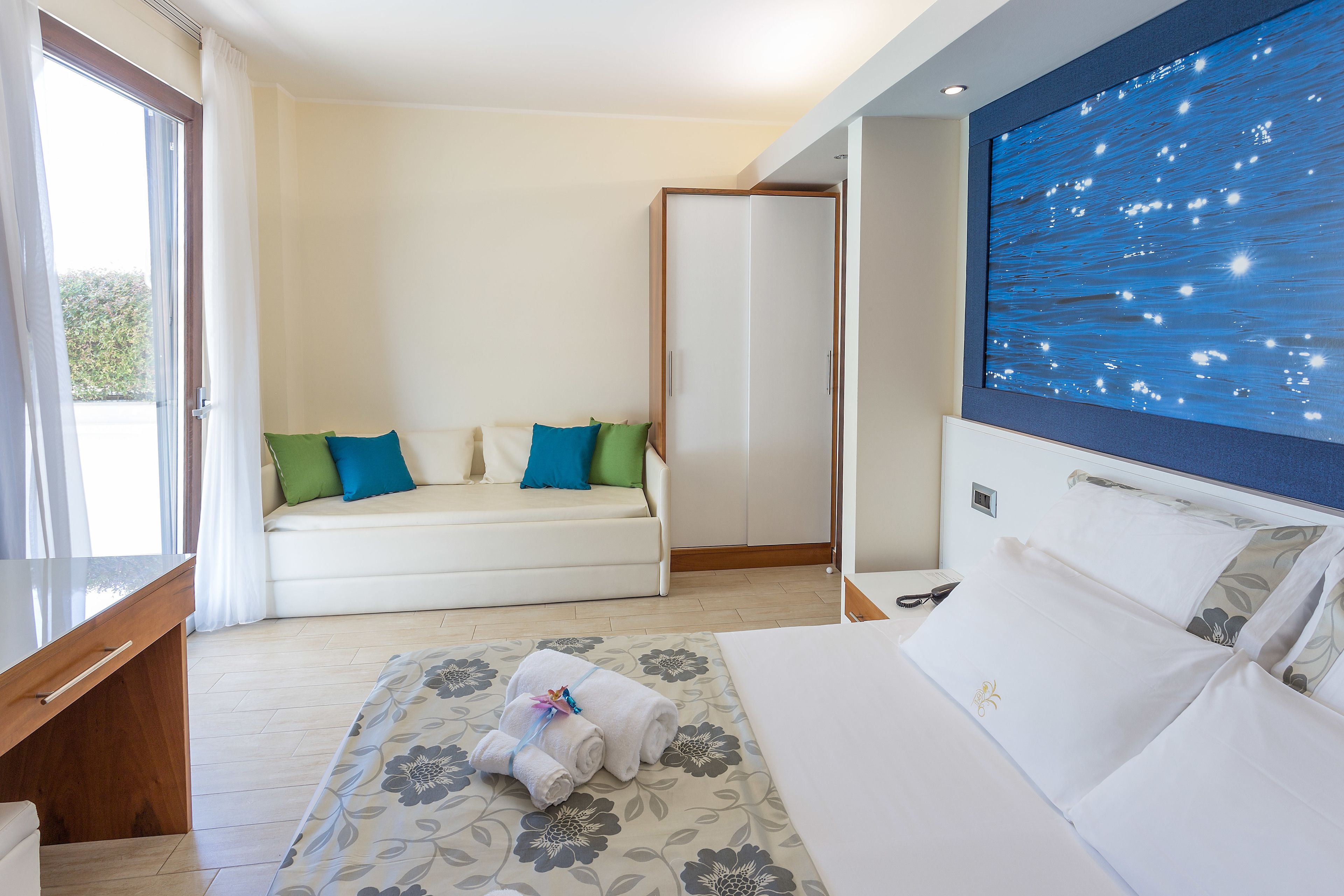 A hotel room with a bed, a sofa, a desk, and a large window.