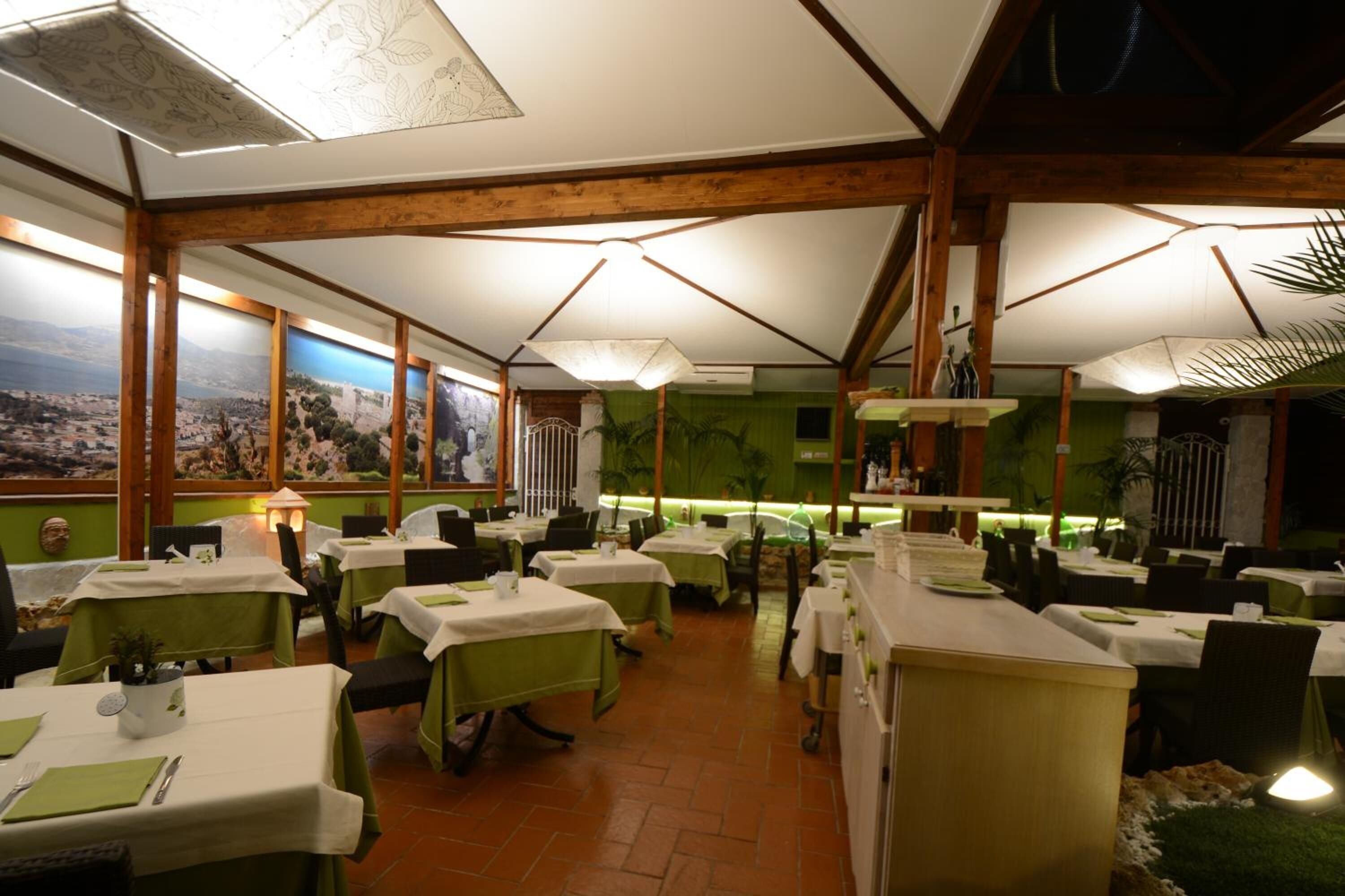 Un restaurante con varias mesas, manteles verdes y vistas a un paisaje a través de amplios ventanales.