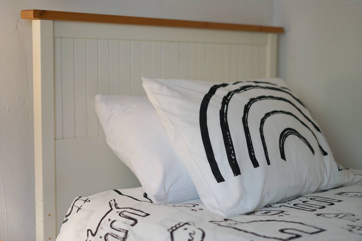 Ein Bett mit weißer Bettwäsche und schwarzen Mustern, ein hölzernes Kopfteil und eine weiße Wand.