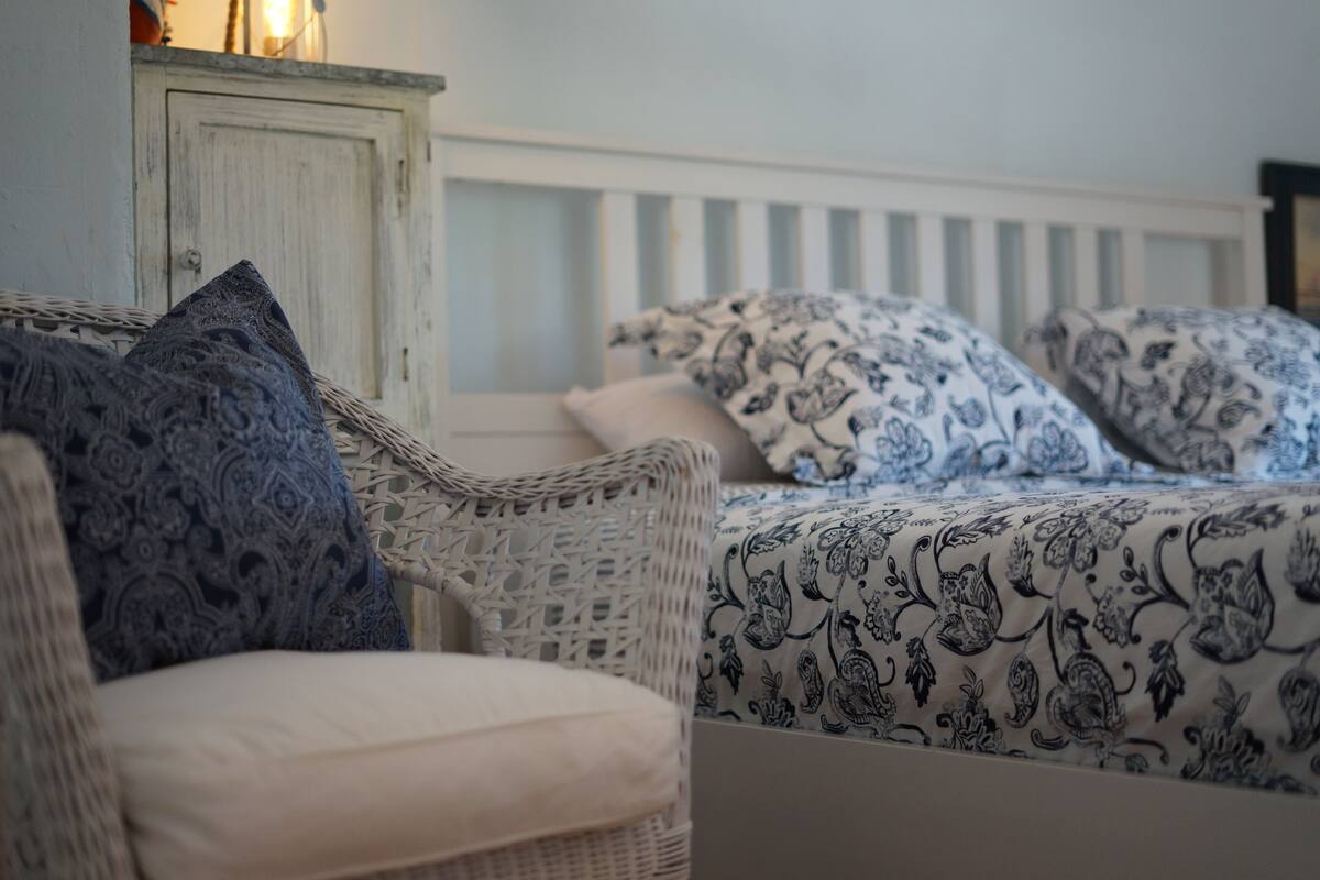 Ein Zimmer mit einem Korbstuhl und einem Bett mit gemusterten Betttextilien.