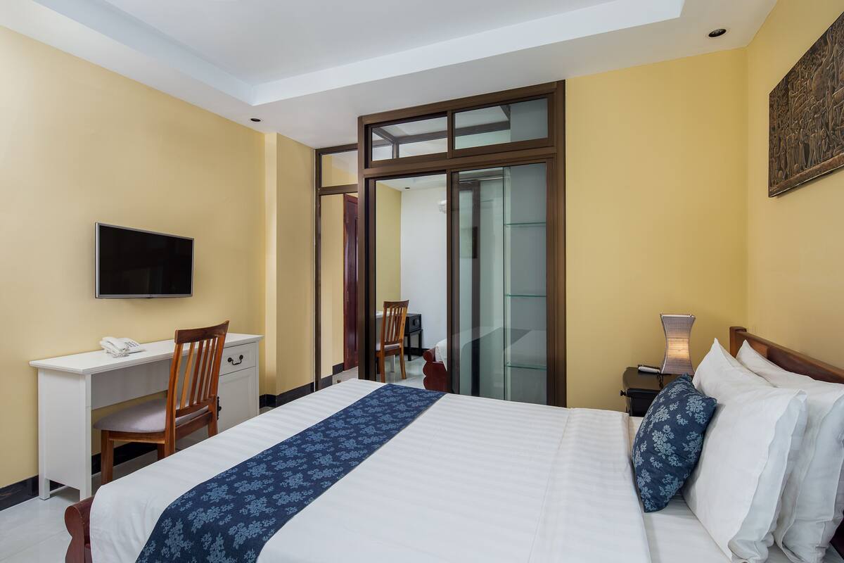 A hotel room with a bed, a desk, a chair, a television, and a sliding glass door leading to a bathroom.