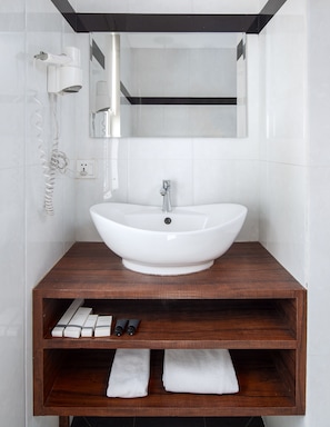 Une salle de bain avec un lavabo blanc, un meuble-lavabo en bois et un sèche-cheveux fixé au mur.