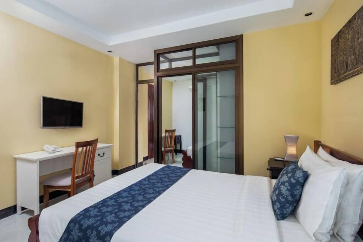 A hotel room with a bed, a desk, a chair, a TV, and a door leading to a balcony.