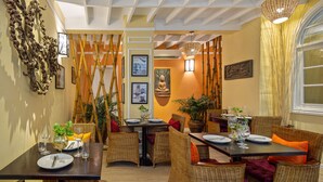 A dining area with wicker furniture, tables set for two, and a Buddha statue in the background. - Botum Palace Hotel (Phnom Penh)