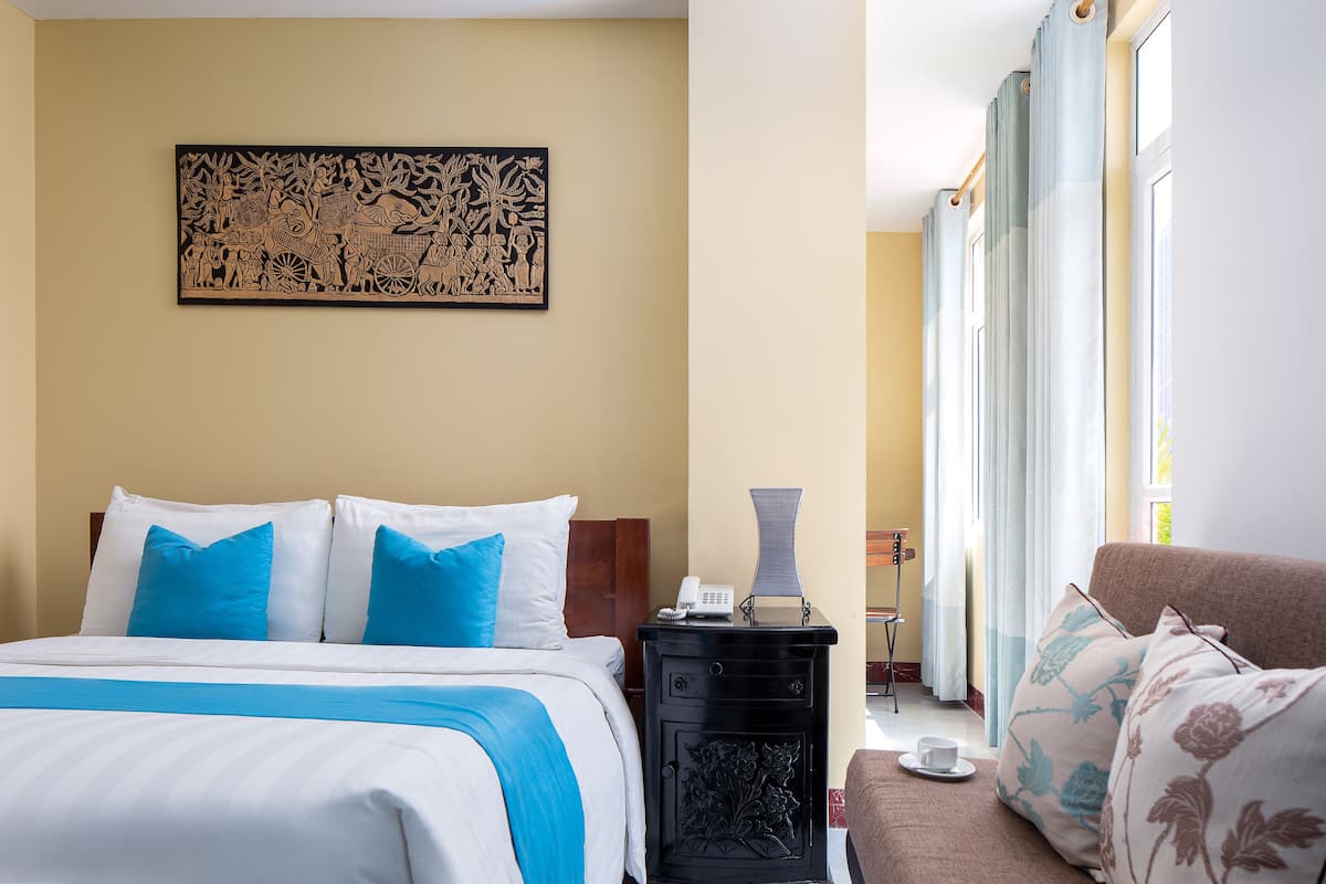 A hotel room with a bed, a nightstand, a lamp, and a window with curtains.