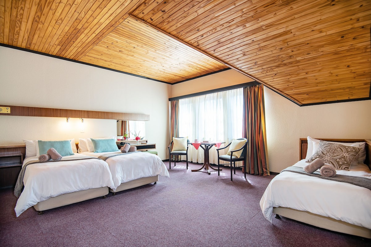 A hotel room with two beds, a small table, chairs, and a window with curtains.