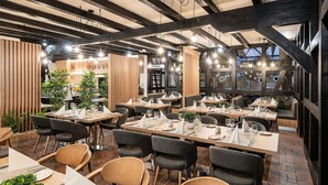 Ein Restaurant mit Holzbalken, moderner Beleuchtung und ordentlich angeordneten Tischen und Stühlen.