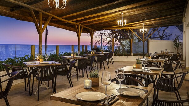 An outdoor dining area with wooden tables and chairs, set against a backdrop of the ocean at dusk. - Hotel Gastronómico La Breña (Barbate)