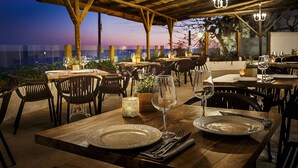 A restaurant with wooden tables and chairs, candlelit tables, and a view of the sunset. - Hotel Gastronómico La Breña (Barbate)