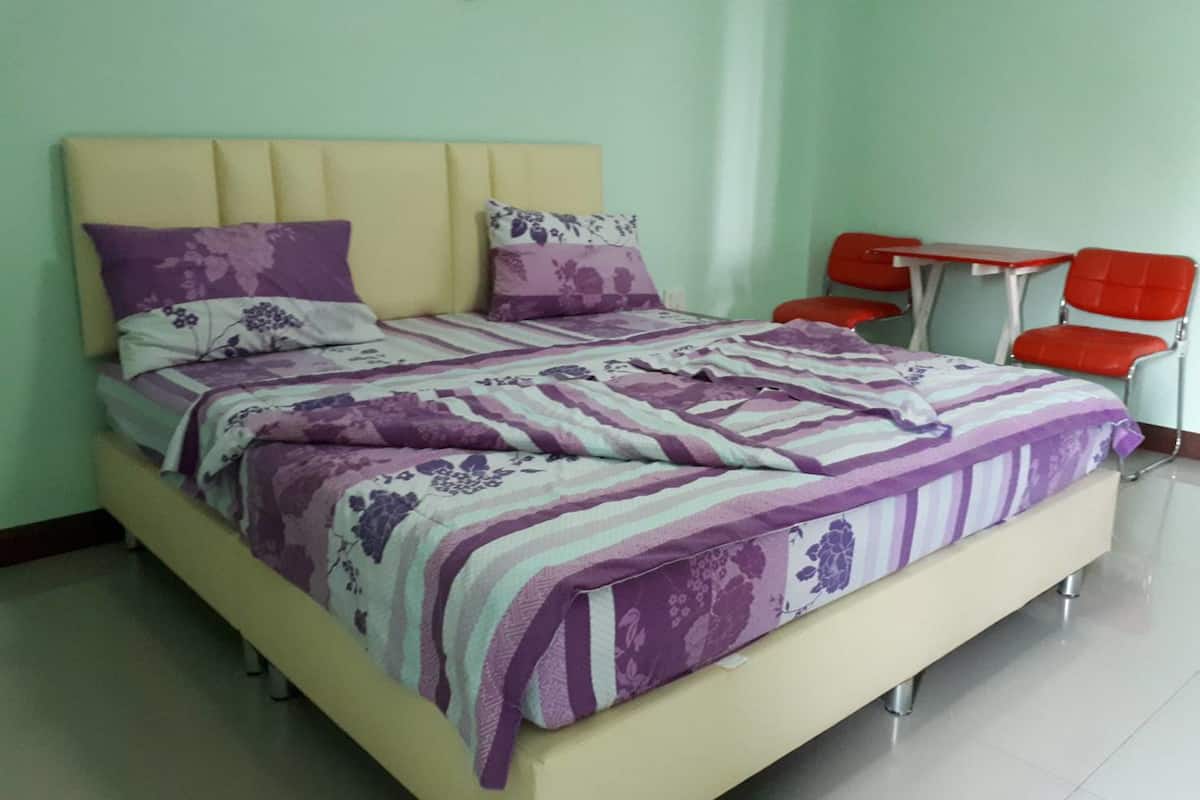 A bed with a floral-patterned bedspread, a headboard, and two pillows. There is a small table with a chair and a lamp on the wall.