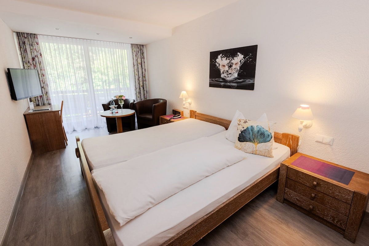 Une chambre d’hôtel avec un grand lit, un bureau avec un ordinateur, une chaise, une petite table avec un vase et un tableau au mur.