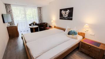 Habitación de hotel con una cama grande, un escritorio con computadora, una silla, una mesita con un florero y un cuadro en la pared.