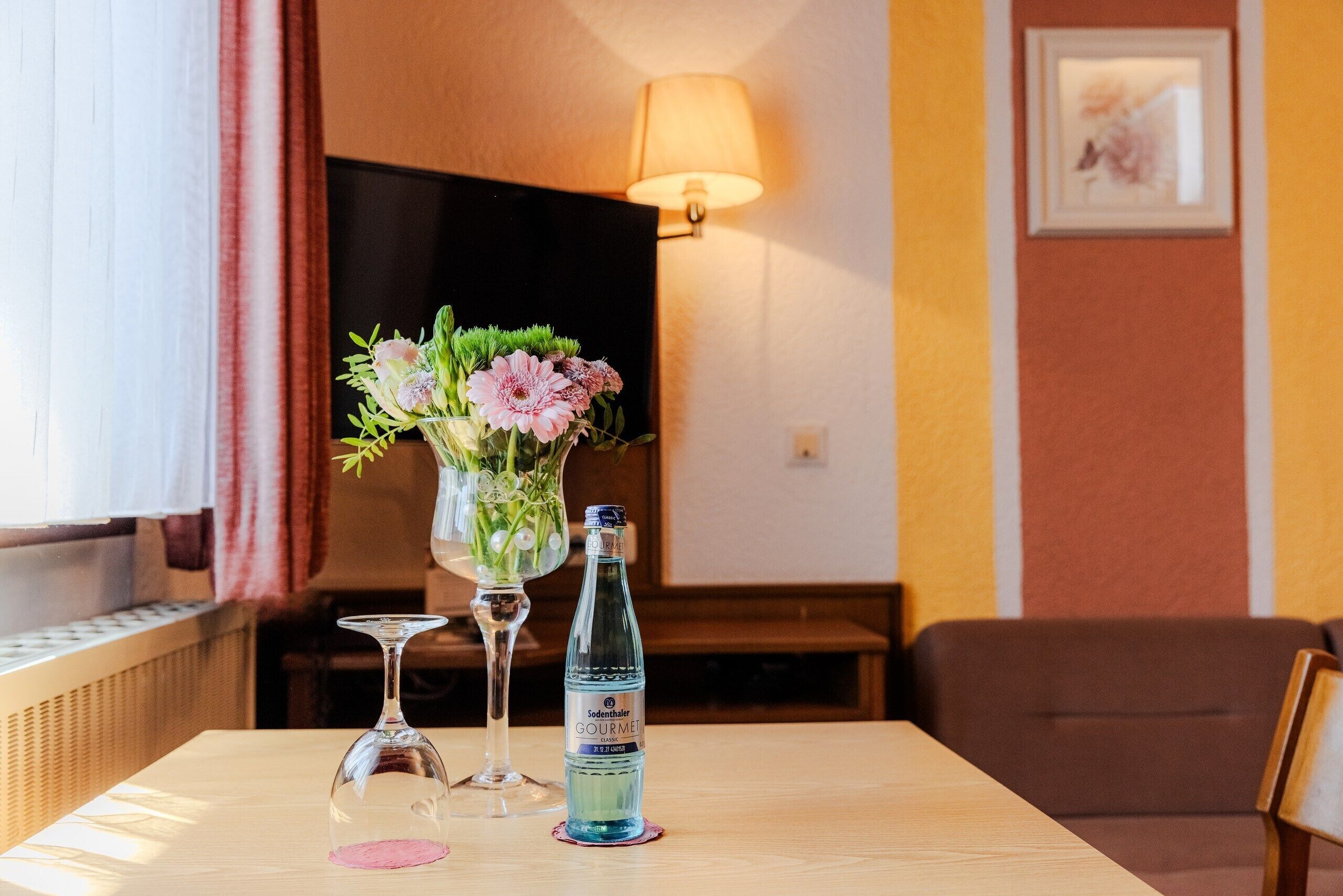 A table with a bottle of water, a glass, and a vase with flowers.