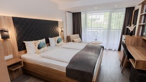 Een moderne hotelkamer met een groot bed, een houten hoofdeinde, nachtkastjes, een klein rond tafeltje en een houten bureau.