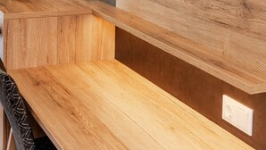 Een moderne woonkamer met een flatscreen televisie bevestigd aan een houten wand, een houten bankje en een vaas met veren van pampasgras.