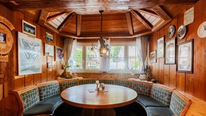 Een houten interieur met een ronde tafel en een bank, ingelijste foto's en een kroonluchter.