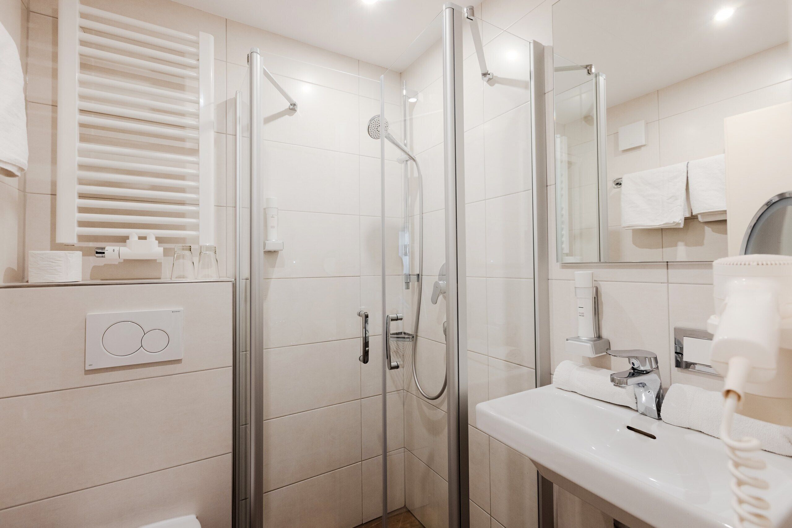 Een moderne badkamer met een douche met glazen wand, een witte wastafel en een spiegel erboven.