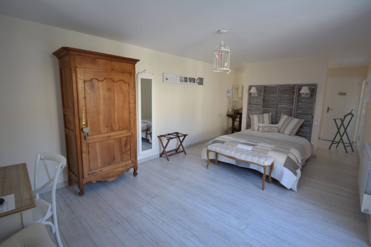 Un dormitorio con un armario de madera, una cama con colcha estampada, una mesita pequeña y una silla.