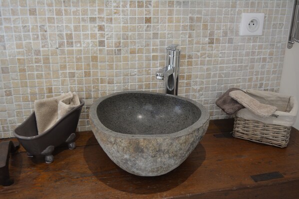 Un baño con lavamanos de piedra, una bañera pequeña y una cesta de mimbre.