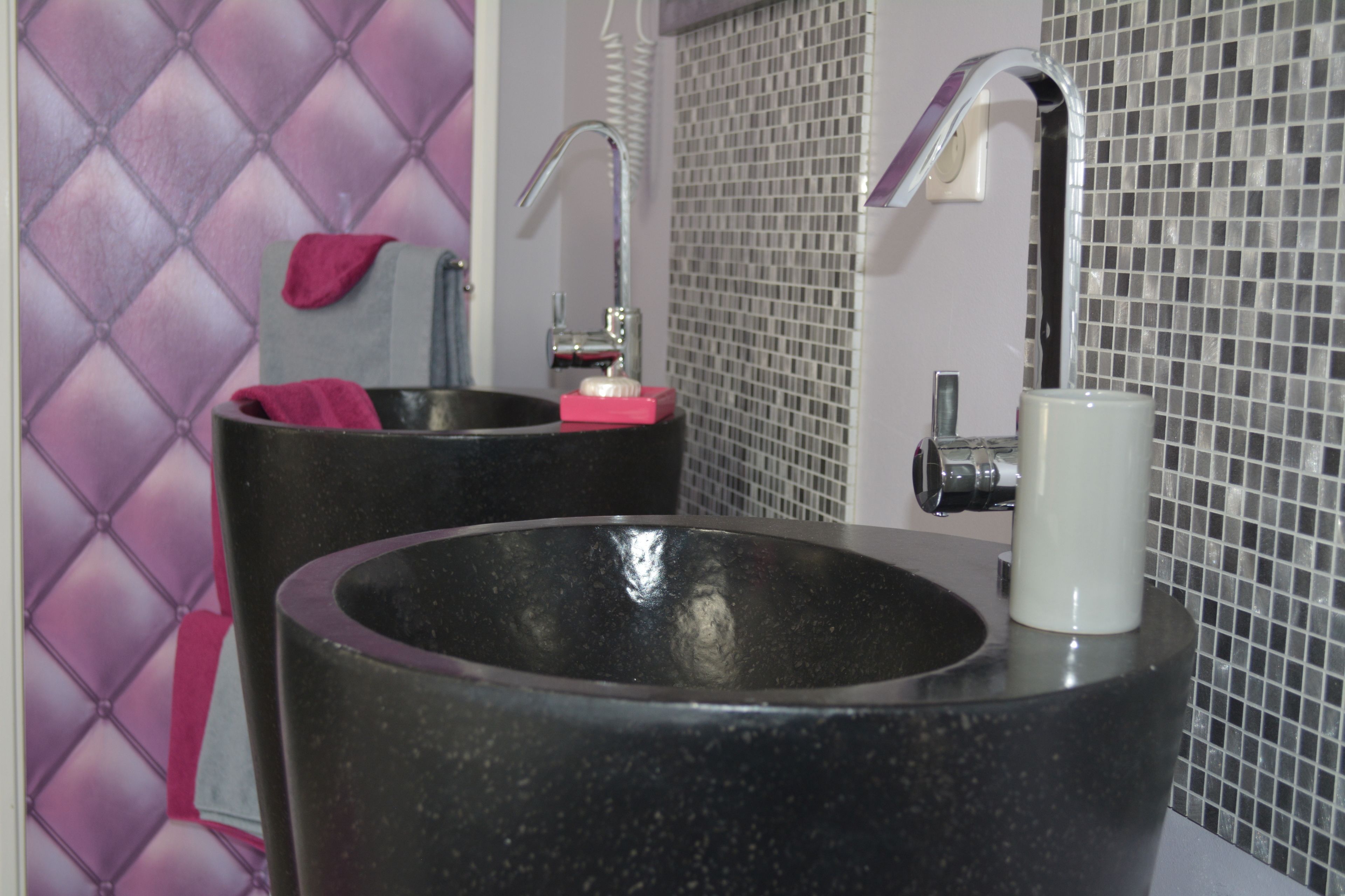 Une salle de bain avec deux lavabos noirs, un miroir et un mur recouvert de carreaux.