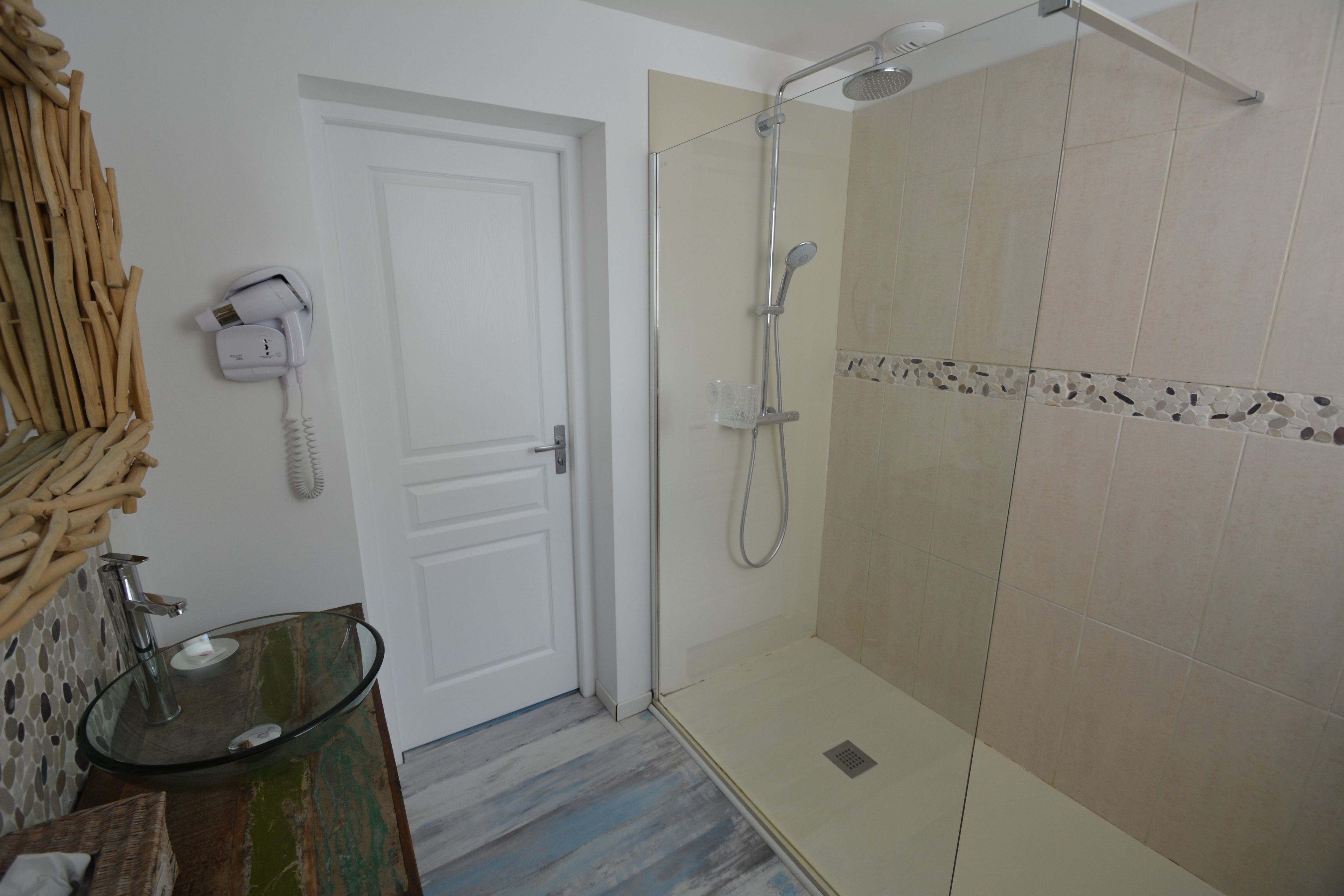 Un baño con lavamanos de vidrio, ducha con cabezal de ducha manual y puerta blanca.