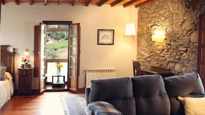 Una sala de estar acogedora con una pared de piedra, un sofá, techo de madera y vistas a través de un ventanal abierto.