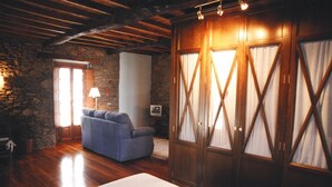 Una habitación acogedora con pared de piedra, vigas de madera en el techo, un sofá y un amplio armario de madera con cortinas.