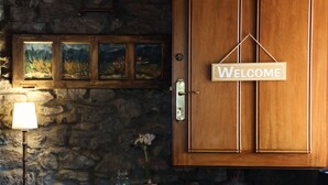 Una puerta de madera con un letrero que dice 'Welcome', un muro de piedra, una lámpara y una pequeña mesa con un jarrón y un libro.