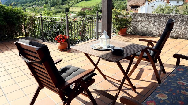 Una terraza con mesa de madera, dos sillas, un farol y una planta en maceta.