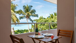 Un balcón con una mesa para dos, con vista a una playa tropical con palmeras y el océano.