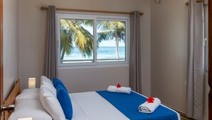 Habitación de hotel con cama, ventana que ofrece vistas a palmeras y al mar, y una barra para cortinas.
