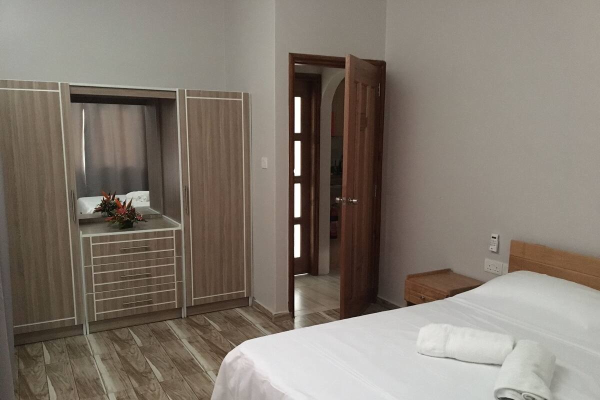 Una habitación de hotel con un armario de madera, una cama con ropa de cama blanca y una mesita de noche pequeña.