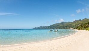 A beach with clear turquoise water, boats, and a sandy shore with greenery in the background. - Shanaz Beachside Retreat (Mahé Island)