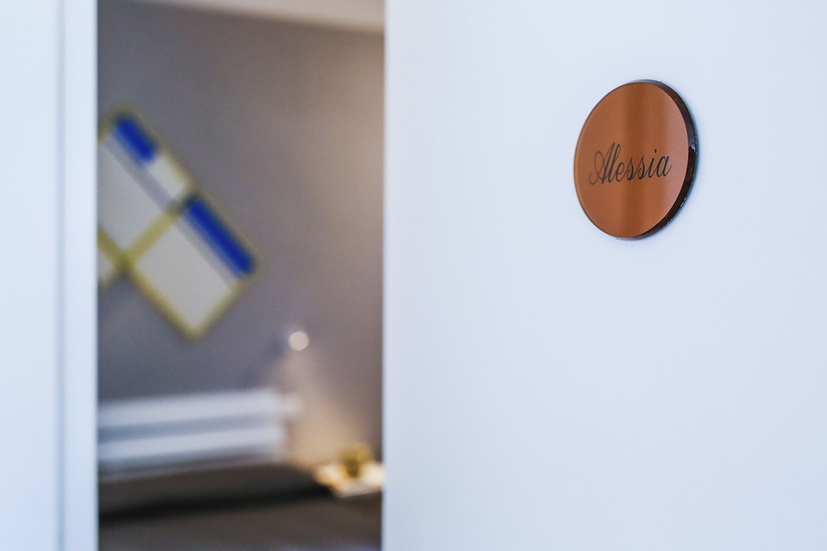 A round, brown sign with the name "Alessia" on a white wall.