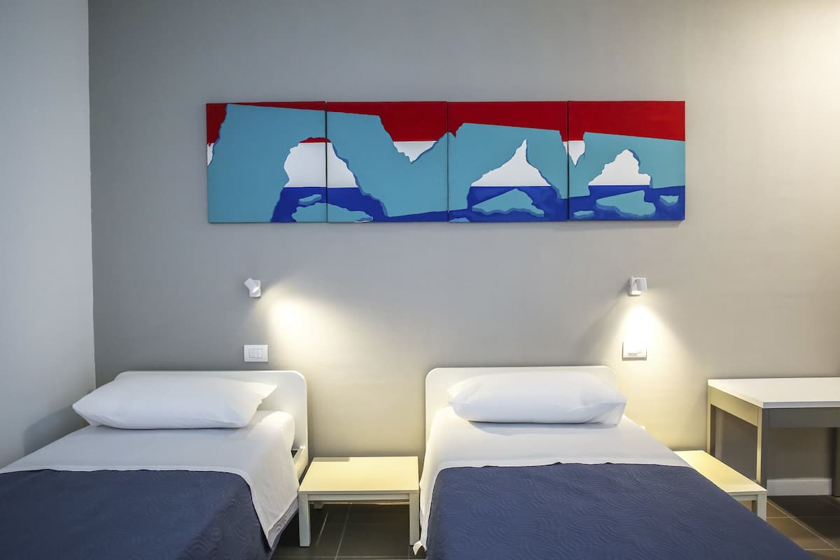 A hotel room with two single beds, a small table, and a wall-mounted artwork.