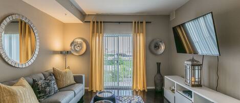 Un salon moderne avec un canapé gris, un tapis à motifs et un téléviseur à écran plat fixé au mur.