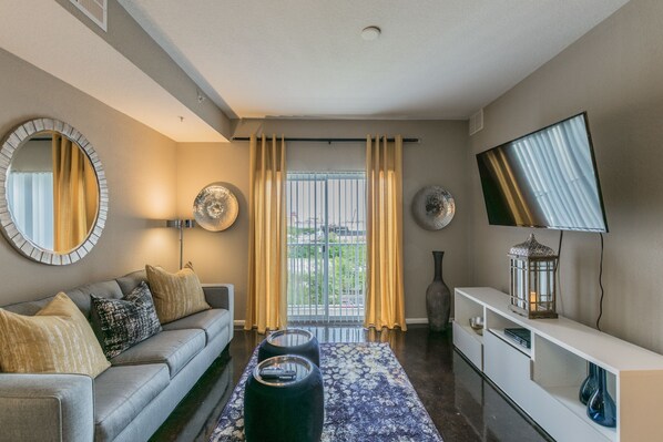 A modern living room with a grey sofa, a patterned rug, and a flat-screen TV on the wall.