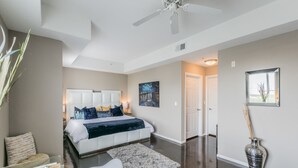 A bedroom with a large bed, a ceiling fan, a night sky painting, and a vase with sticks.