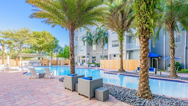 A pool area with lounge chairs, palm trees, and a building with balconies.