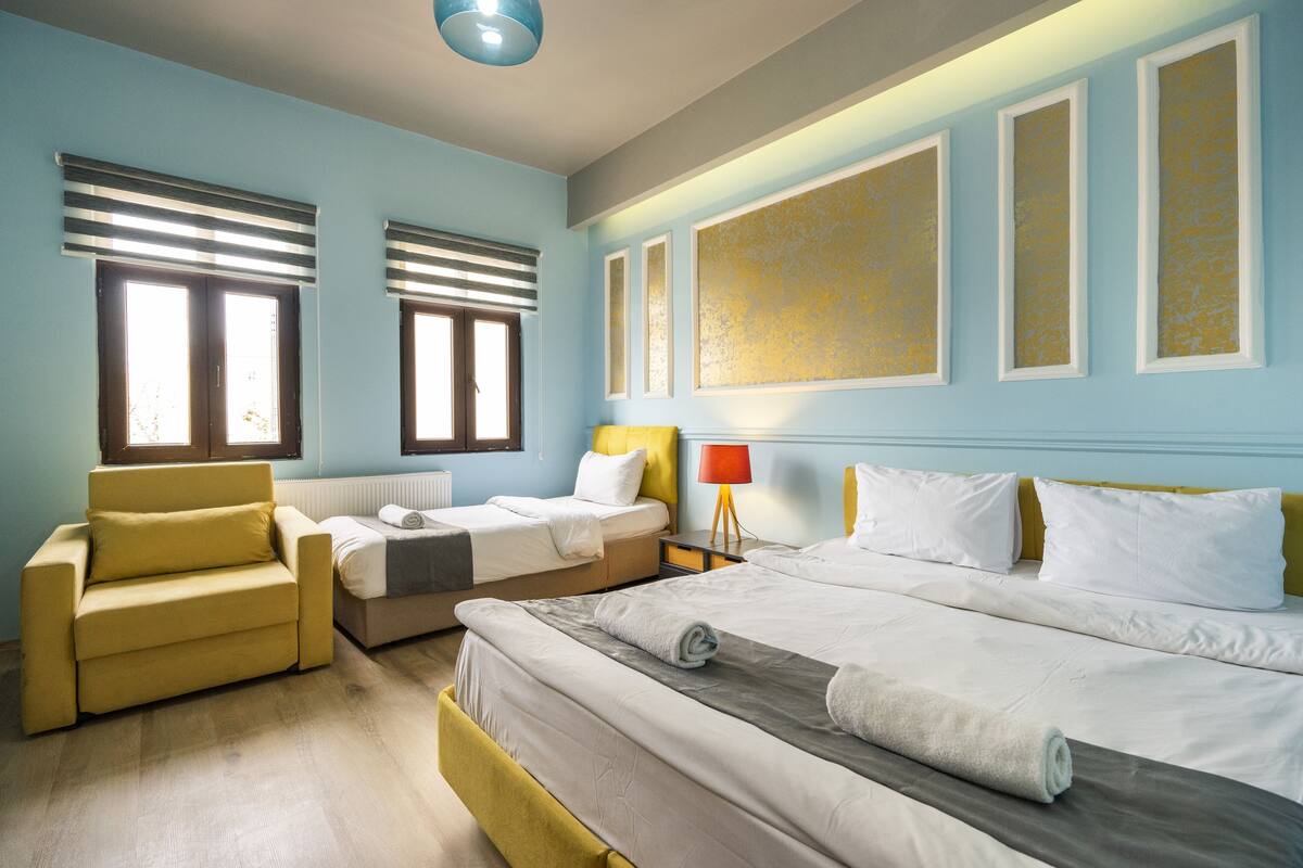 A hotel room with two single beds, a sofa, a nightstand, and a lamp.