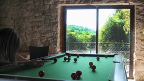 Une table de billard avec des billes, une fenêtre donnant sur un paysage verdoyant et un mur en pierre.