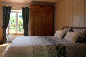 A bedroom with a large bed, a wooden wardrobe, and a window with curtains. - Moulin Pont Vieux - Chambres d'Hôtes (Mortagne-sur-Sevre)