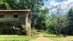 Un chalet rustique, accessible par un chemin de terre, entouré d’une végétation luxuriante et d’arbres.