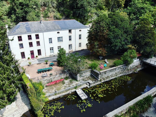 A white building with multiple windows and a red door, surrounded by greenery and a small water body. - Moulin Pont Vieux - Chambres d'Hôtes (Mortagne-sur-Sevre)