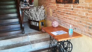 Un escalier avec une rampe en bois, un mur de briques orné d’un tableau, une table avec une bouteille et une machine à coudre.