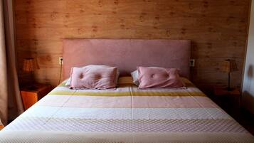 A bedroom with a wooden headboard, two pink pillows, a patterned bedspread, and a bedside table with a lamp.