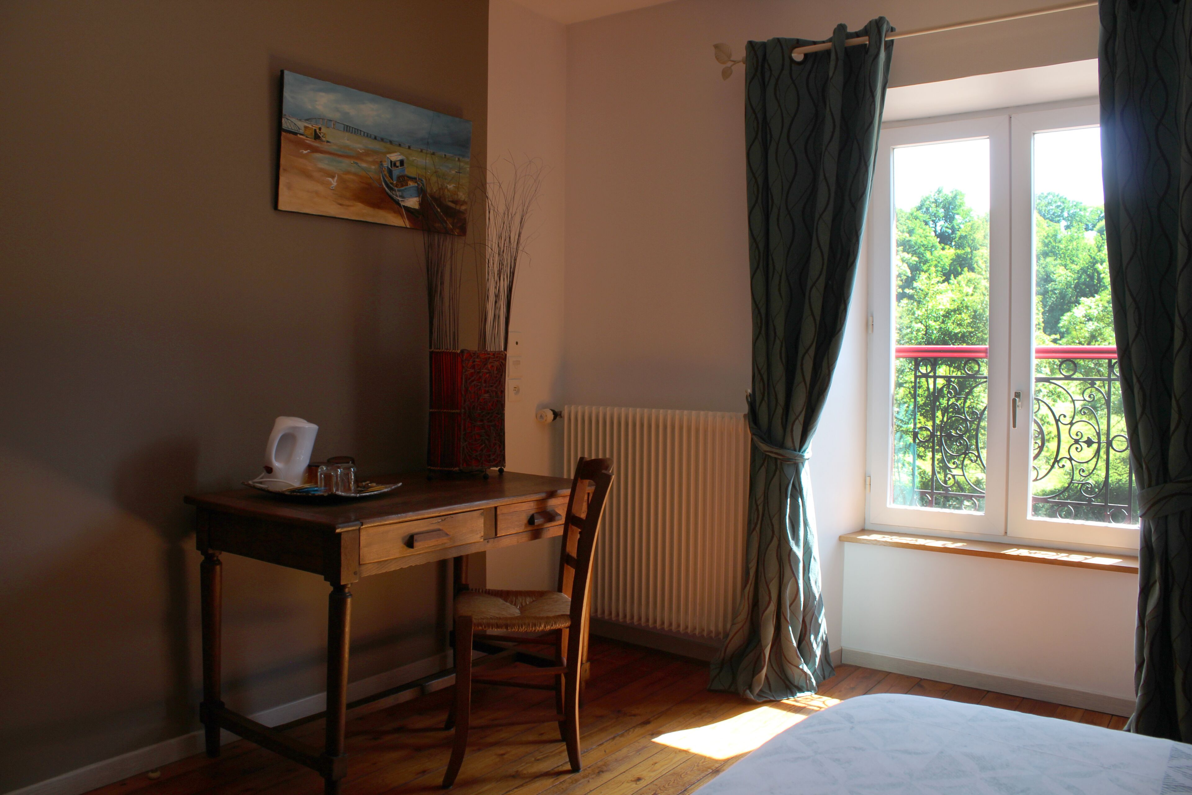 Une chambre avec un bureau en bois, une chaise, un radiateur, une fenêtre avec des rideaux et un tableau accroché au mur.