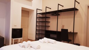 A hotel room with a bed, a desk, a TV, and a black shelving unit. - Cairoli Rooms (Rome)