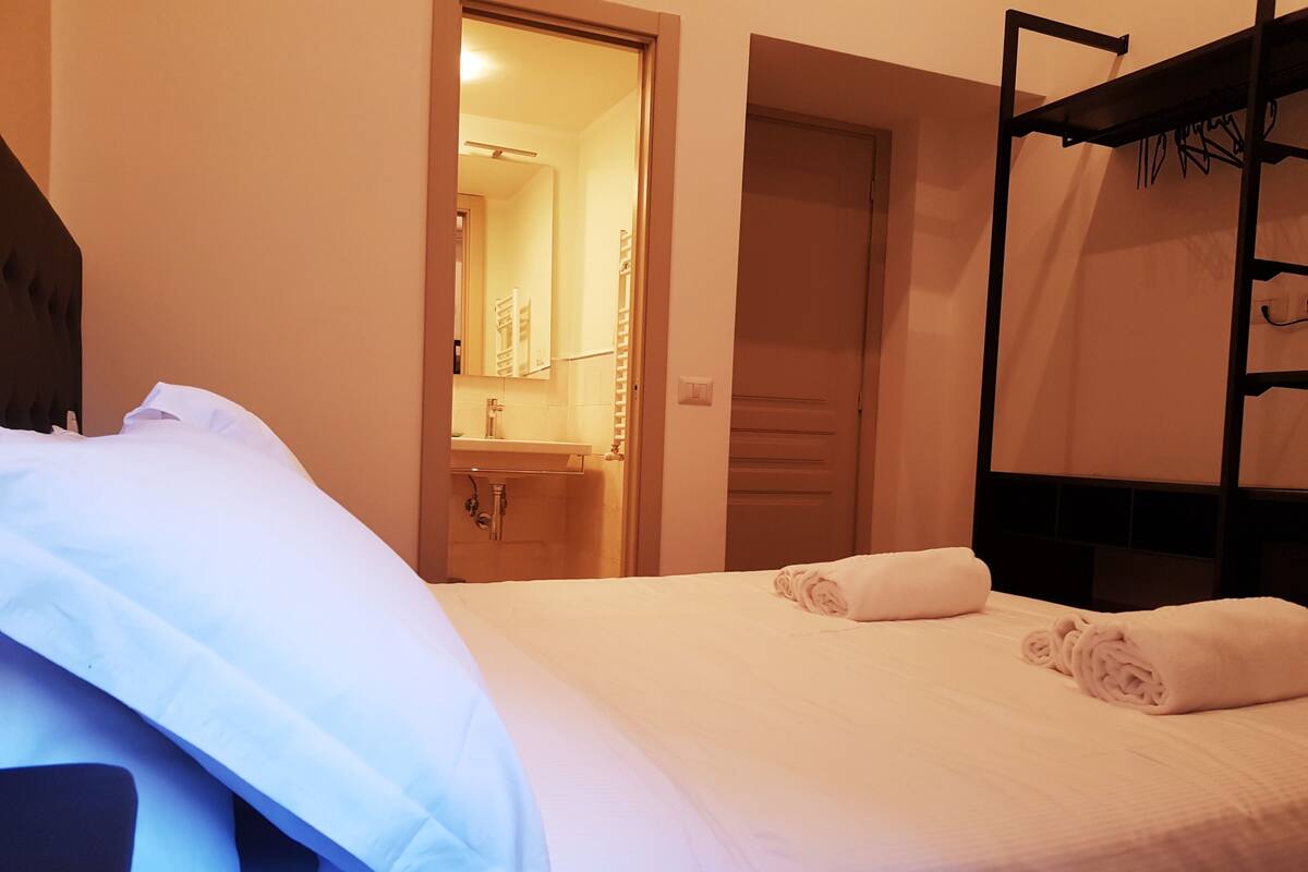 A hotel room with a bed, a bathroom with a sink and mirror, and a bunk bed.