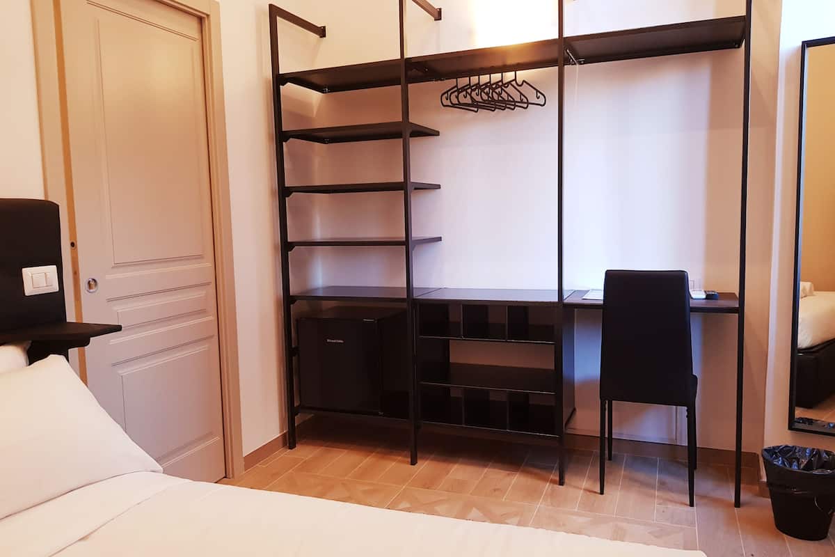 A compact bedroom with a bed, a desk, and a wardrobe with shelves.
